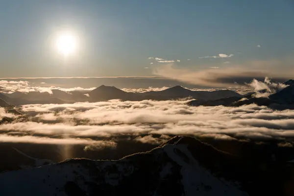 青空の明るい太陽の光線は 夜明けに完全に霧の流れで覆われている山のマスコグラを照らしました — ストック写真