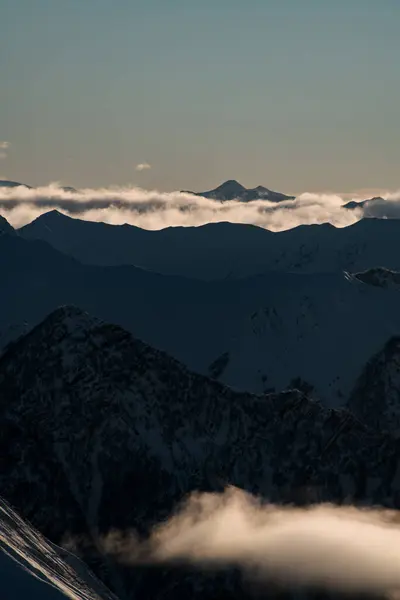 岩石群山的尖峰在明亮的天空背景下清晰可见 浓雾从山坡上滑落下来 — 图库照片
