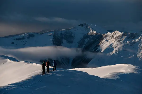 三位男子滑雪者站在雪地的斜坡上 欣赏着一辆山地车 它的一部分被一小群雾所覆盖 — 图库照片