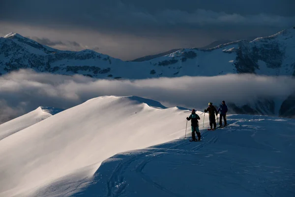 三个男子滑雪者爬上一座雪山 环顾四周 发现后面是一座被雾覆盖的高山 — 图库照片