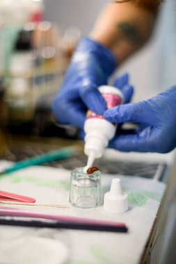 Mavi lateks eldivenli kadın elleri kaş boyasını karıştırmak için cam bardağa boya sıkıyor.