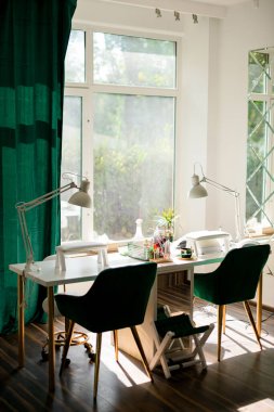 İki iş yeri için tasarlanmış bir güzellik salonunda, manikür aletleri ve masa lambalarıyla uzun beyaz bir masa.