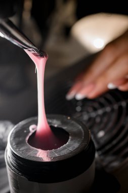 Manikürcü elleri, müşterilere uygulamak için kavanozdaki pembe jöleyi fırçadan alır.