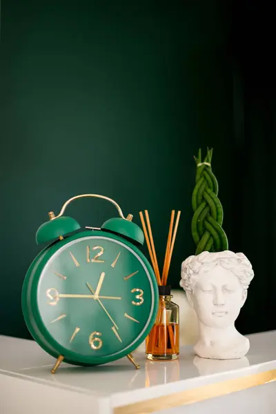 At the reception of the beauty salon there are a clock, a statuette and a jar with scented sticks as decorations