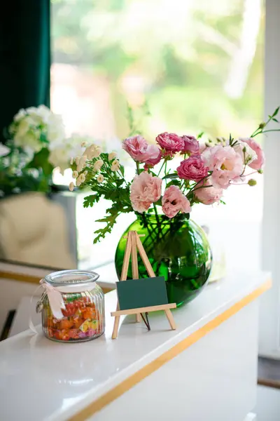 Business card, flowers in a glass vase and a jar with candies stand as decorations at the reception of the beauty salon