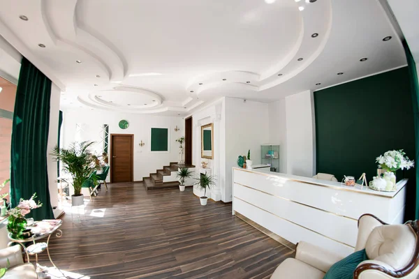 Multi-story hall of a beauty salon with a reception desk, decorated in a white style with elegant armchairs, a coffee table and other decorations