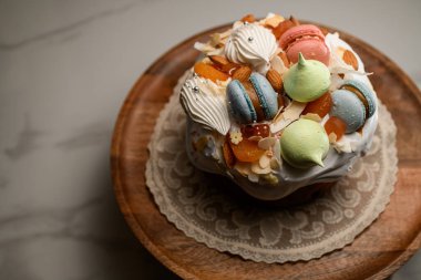 Beyaz kremalı turta, mavi-pembe kurabiyeler, şekerli meyveler ve badem dolgulu ve ahşap bir standda narin krema.