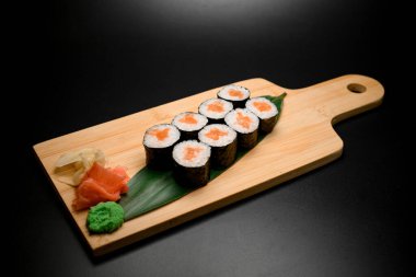 Somon, zencefil ve wasabi 'li lezzetli suşi dürümleri siyah arka planda izole edilmiş ahşap bir tahtada servis edilir.