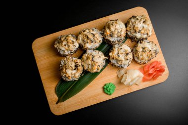 Sushi rulo susam tohumu, kızarmış karides eti ile kaplanmış zencefil ve wasabi ile süslenmiş ahşap bir tahtanın üzerinde
