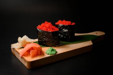 Kırmızı havyarlı suşi ruloları, zencefil, wasabi ve ahşap bir tahtada muz yaprağı ile süslenmiş.