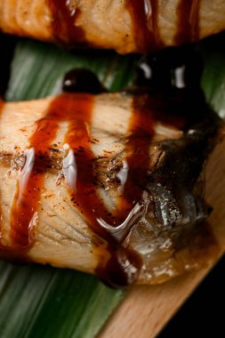 Tahta tahtada muz yaprağına sos serpiştirilmiş somon dilimlerine sarılmış ruloların yakın plan fotoğrafı.