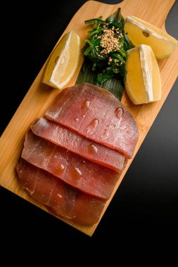 Düz ton balığı fileto dilimleri, kabuklu limon dilimleri ve susamlı deniz yosunu ıssız bir tahta üzerinde uzanıyor.