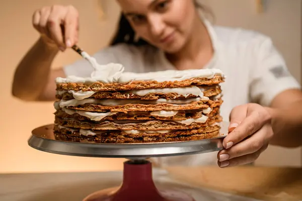 穿着白色工作服的装卸工做一个蛋糕 蛋糕架上的糕点上涂着厚厚的 油腻可口的奶油 — 图库照片