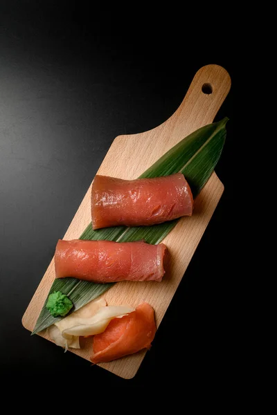 Rolls wrapped in salmon slices on banana leaf with ginger and wasabi on a wooden board isolated