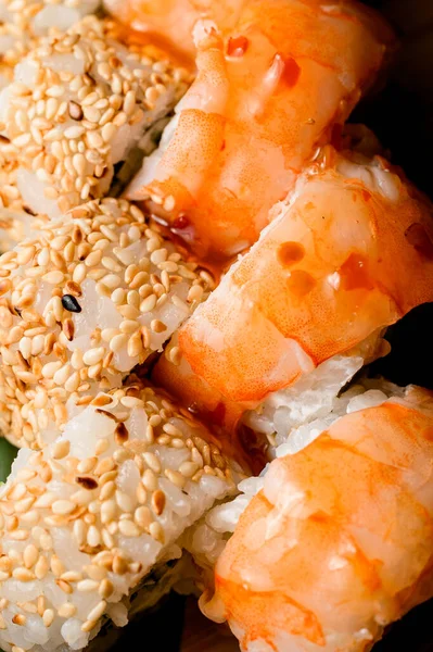 Cropped close-up photo of two kinds of delicious sushi rolls covered in sauce and sprinkled with sesame seeds, top view
