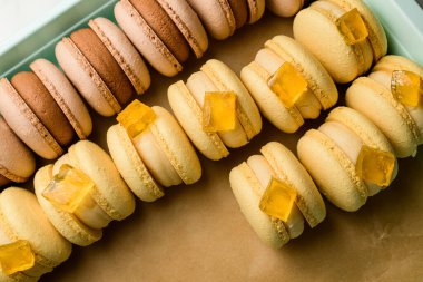 Açık dikdörtgen cam kapta kahverengi parşömen kağıdıyla kaplı bej ve kahverengi kremalı badem kurabiyelerinin üst görüntüsü