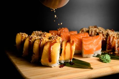 Philadelphia suşisi üzerine sushi tohumları serpiştirilmiş somon, ton balığı ve maki ile suşi ruloları serpiştirilmiş.