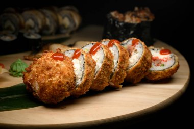 Diğer suşi rulolarının bulanık arka planında ketçap damlalarıyla kızarmış suşi rulolarını kapatın.