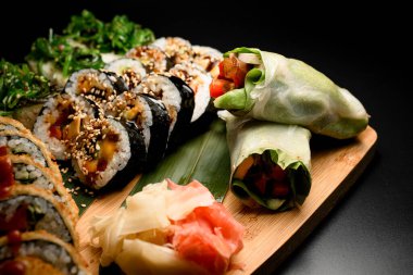 Sebze, balık ve krem peynirli böreklere odaklan ve susamlı suşi ruloları ahşap bir tahtanın üzerine zencefil serpiştir.