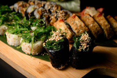 Susam serpiştirilmiş Gunkan 'a odaklan. Suşi rulolarının geri kalanı bulanık arka planda, ahşap tahtada uzanıyor.