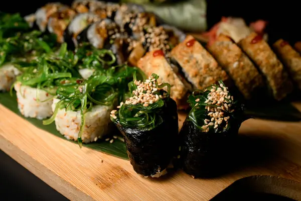 Susam serpiştirilmiş Gunkan 'a odaklan. Suşi rulolarının geri kalanı bulanık arka planda, ahşap tahtada uzanıyor.