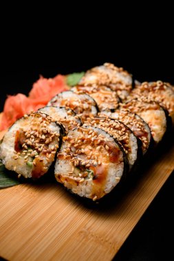 Unagi sosuyla kaplanmış suşi rulolarının ön planına odaklan ve üzerine susam tohumları serp, ahşap bir tahtada wasabi ve zencefil serp, yakın plan.