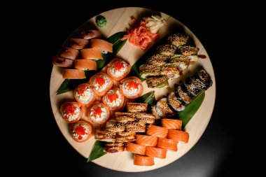 Wasabi ve zencefilli suşi dürümleri, siyah arka planda, ahşap bir tahta üzerinde servis edilir.