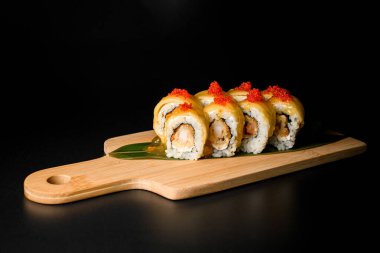 Sarı sosla kaplı suşi rulolarının yan görüntüsü ve ahşap bir tahtanın üzerinde kırmızı havyarla kaplanmış.