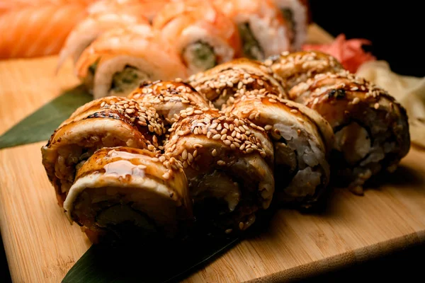 Focus on fried sushi rolls with tuna covered with sauce and sesame seeds on a wooden board, the rolls are blurred behind
