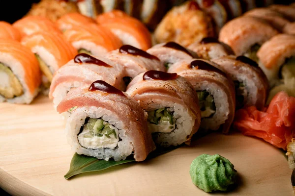 Focus on sushi rolls with tuna garnished with drops of brown sauce, garnished with wasabi and ginger, other types of sushi rolls on blurred background