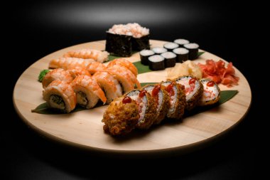 Siyah arka planda wasabi, beyaz ve kırmızı zencefilli muz yaprakları üzerinde uzanan bir dizi suşi rulosunun ön planına odaklan.