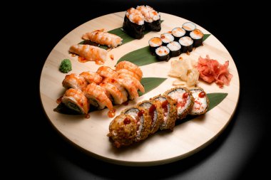 Siyah arka planda, yuvarlak bir tahta üzerinde muz yapraklarıyla süslenmiş suşi rulolarının üst görüntüsü.