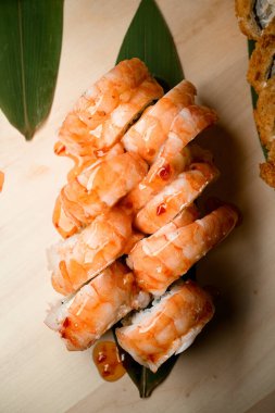 Altın şeffaf sosla kaplanmış ve muz yapraklarıyla süslenmiş bir karides suşi setinin üst görüntüsü.