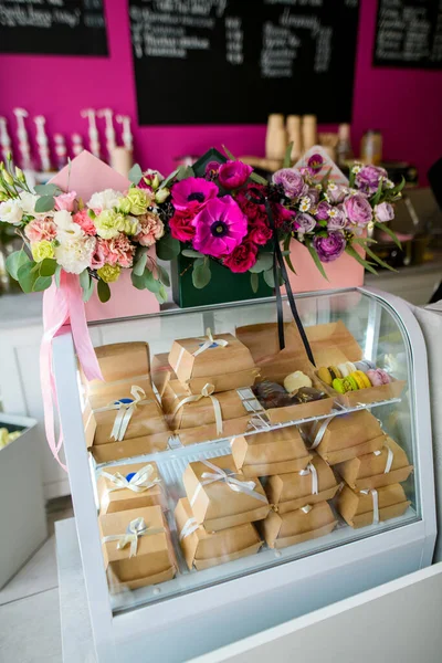 Bouquets in gift boxes and brown boxes for gift wrapping stand in the window of a flower shop against a pink wall background
