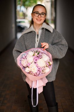 Elinde pembe şakayık buketi ve kurdeleli pembe ambalajlı çingene çiçekleri tutan genç bir kadın.