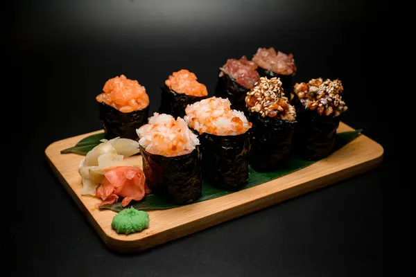 assortment of finely chopped fish products thoughtfully arranged on a leaf, accompanied by zesty ginger and pungent wasabi for a diverse seafood experience.