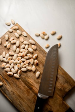 Düzgün soyulmuş badem koleksiyonu sanatsal olarak tahta bir kesme tahtasının üzerinde bıçakla sunuluyor.