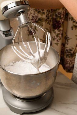 Beyaz mutfak masasında cam kase çırpılmış yumurta beyazı kreması.