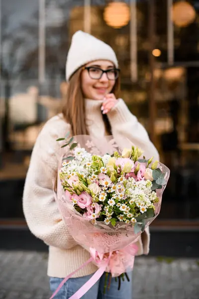 Uzun saçlı genç kız, elinde Eustoma çiçekleri, papatyalar ve okaliptüs karışımı narin bir karışım tutuyor. Çiçek buketine odaklan. Çiçekçi dükkanı konsepti