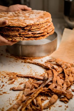 Fırıncı, kırpılmış yuvarlak pastayı, kenarları budanmış ve yuvarlak metal tavalı boş masaların üzerinde tutar.