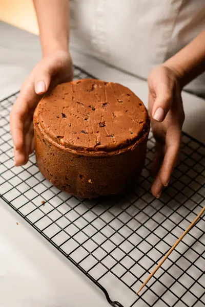 Baker, Paskalya pastasını elinde tutuyor. Pasta mutfak masasının üzerinde duruyor.