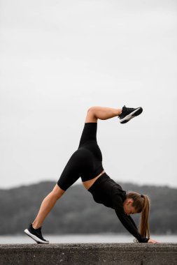 Resimli deniz sahili ortamında, genç ve sağlıklı bir kız dinamik esneklik ve maharet sergiliyor..