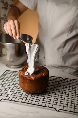 Beyaz elbiseli bir kadın, paskalya pastasına krema sürüyor.