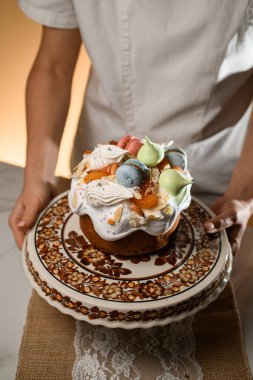 Güzel dekore edilmiş Paskalya pastası bir halk süsüyle ayakta duruyor, güzel bir kadın fırıncı yakınlarda duruyor.