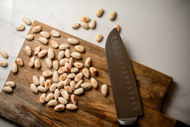 Beyaz mutfak masasında kavrulmuş kabuklu fıstıkla ahşap kesme tahtasının üzerinde keskin büyük bir bıçak.