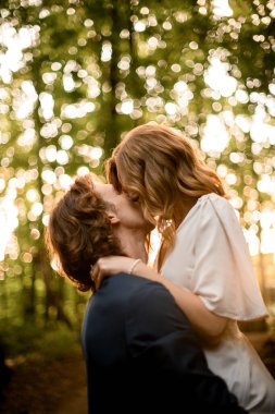 Adam karısını kollarına alır ve ormanın arka planında dikilirken öpüşürler.