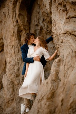 Kadın kocasına sırtını döner ve başını ona doğru çevirir. Onu dik bir uçurumun kenarında öper.