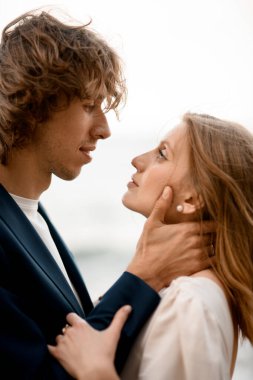 Yeni evliler birbirlerinin gözlerinin içine bakar. Deniz ve gökyüzünün arka planına bakarlar. Koca, karısının boynunu nazikçe tutar.