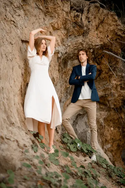 Serious man and his wife are standing near a steep cliff, looking into the distance in different directions