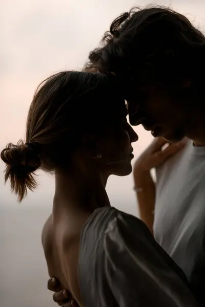 Wife with her hair in a bun stands in the arms of her husband, touching their foreheads to each other close-up